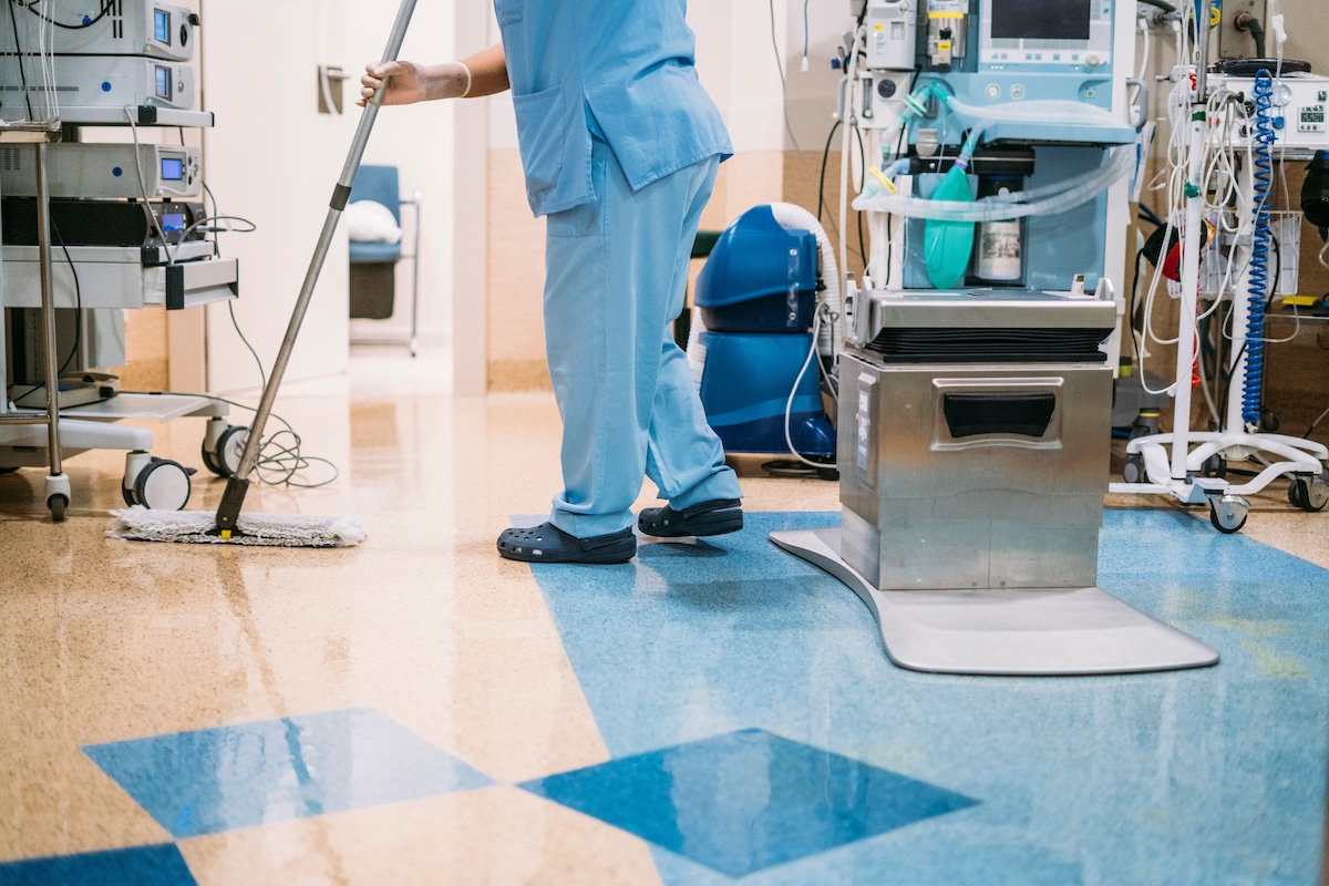 Medical office cleaning specialist in PPE sanitizing a clinical surface
